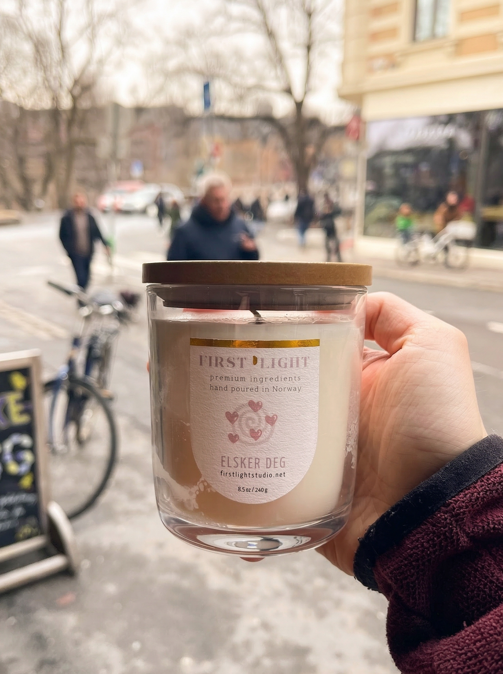 Hand holding a candle labeled 'First Light' on a city street.
