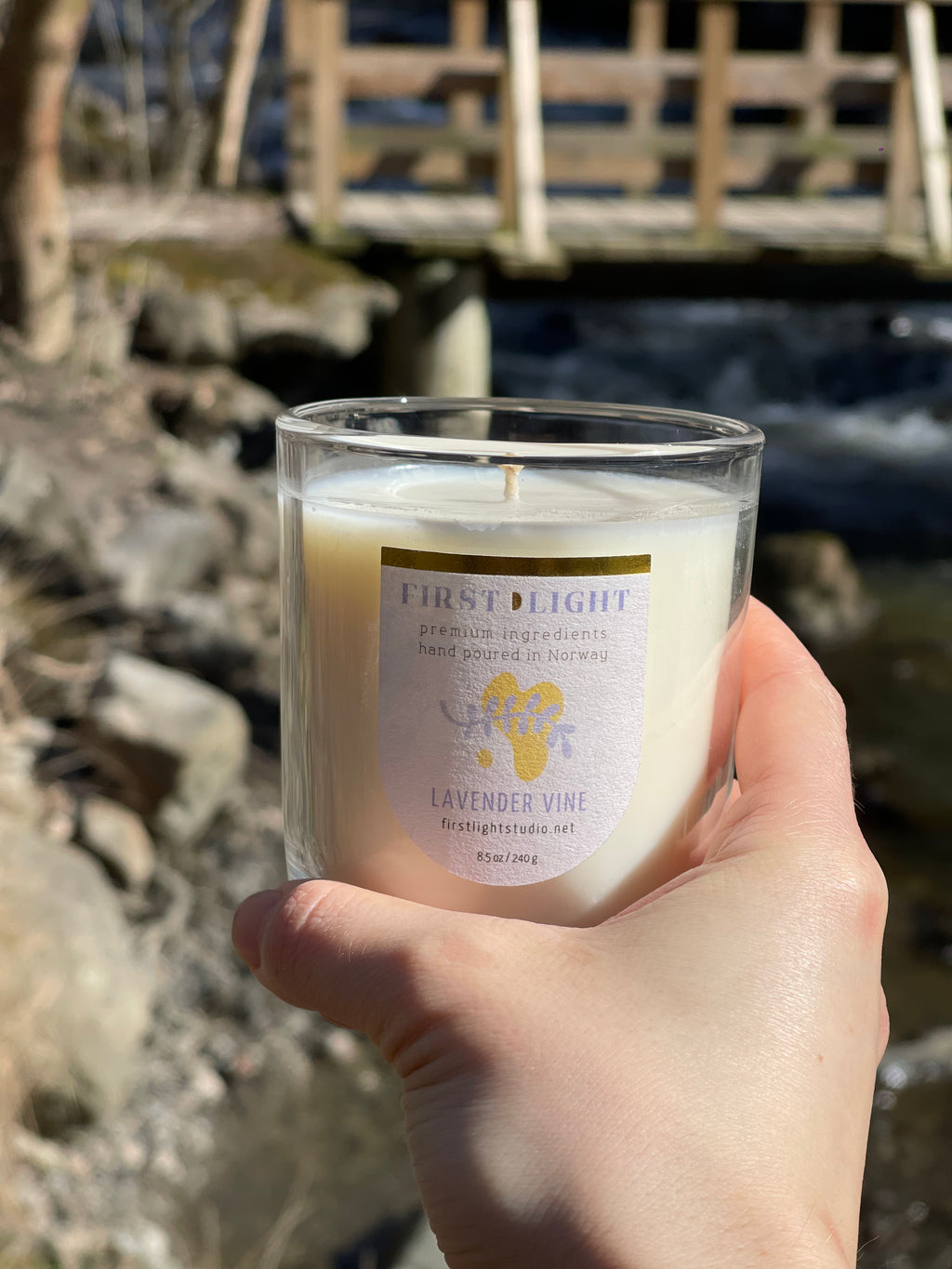 Hand holding a candle labeled 'First Light' with a natural background