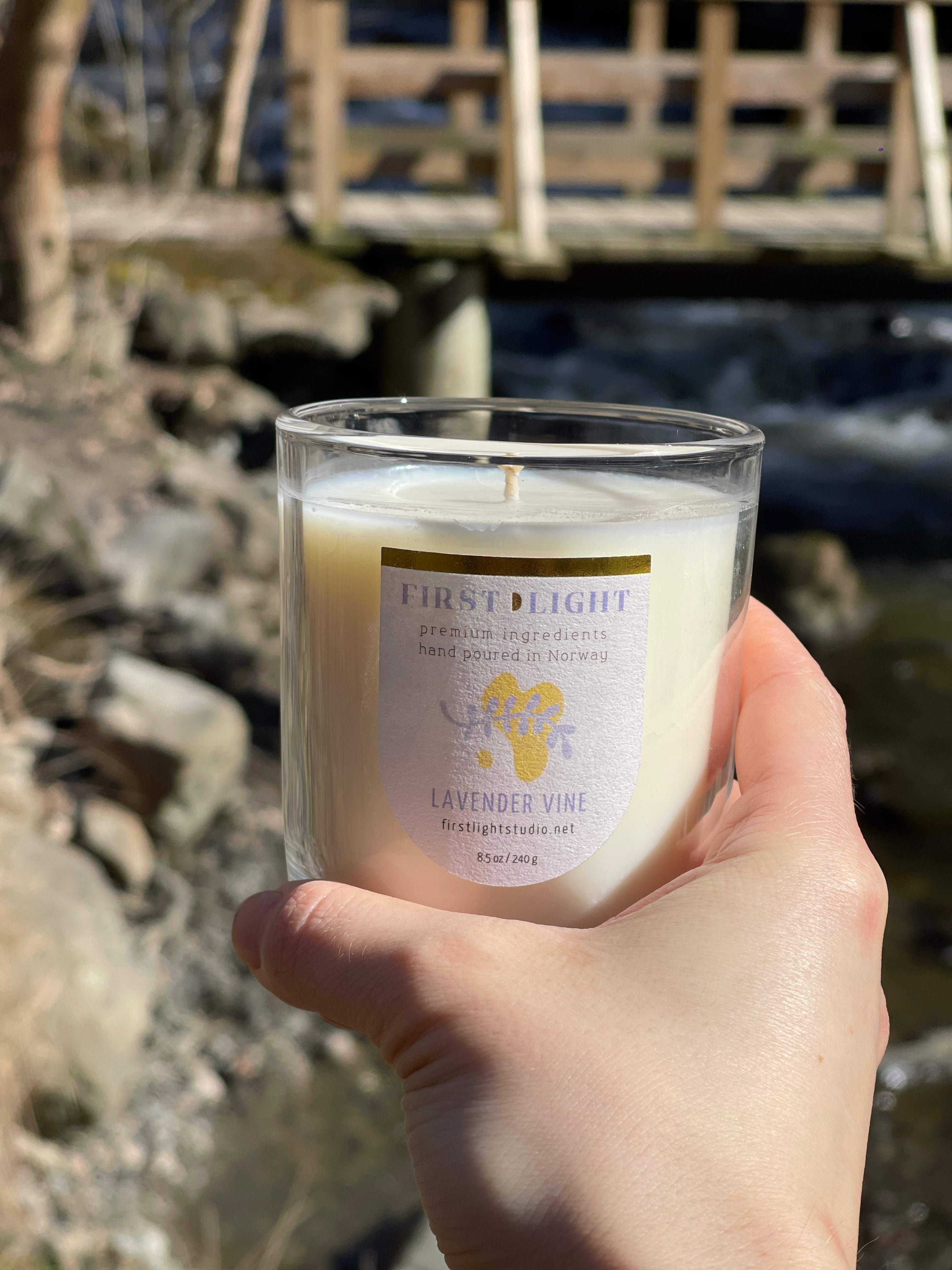 Hand holding a candle labeled 'First Light' with a natural background