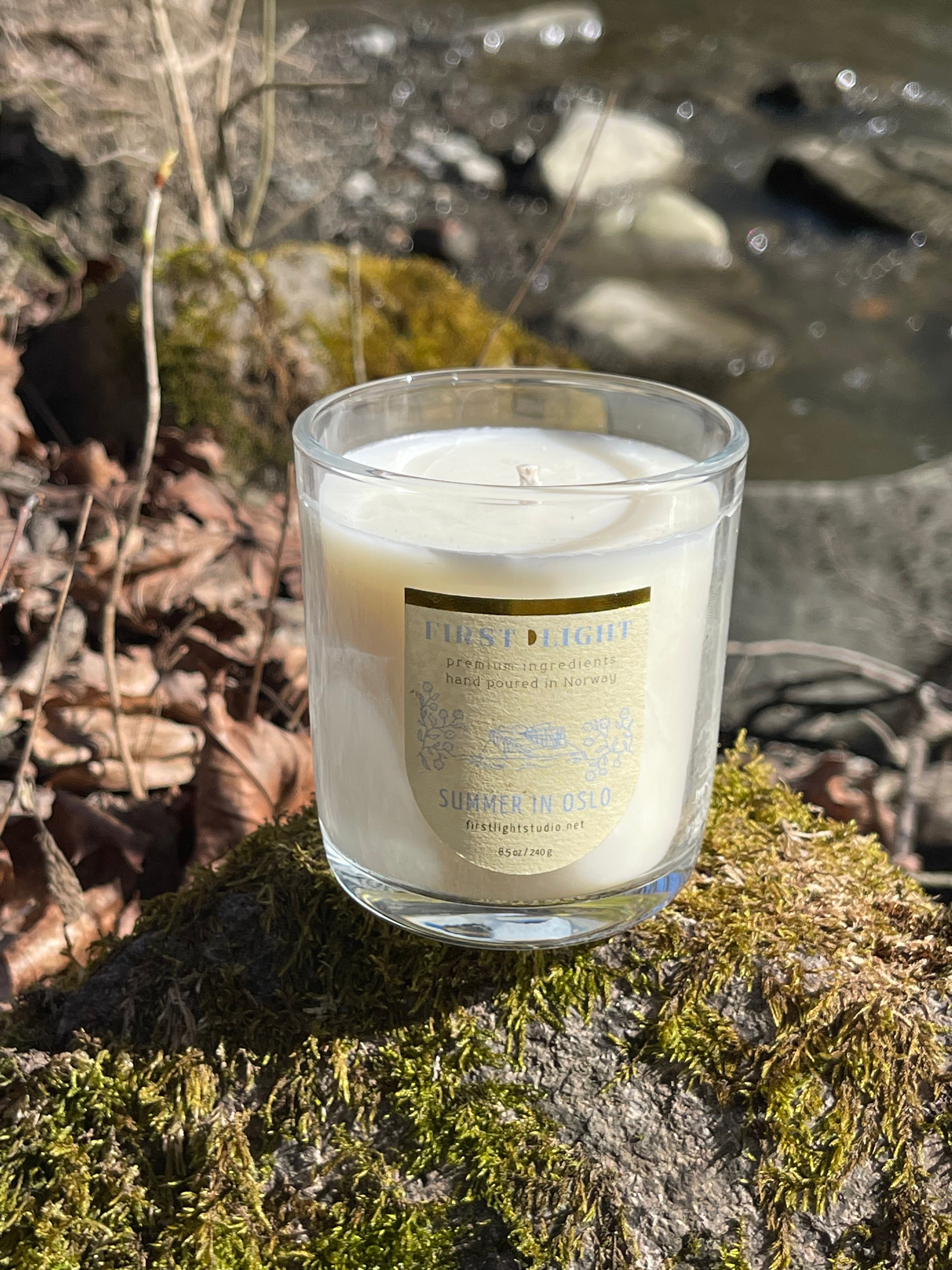 Candle in a glass jar with a label on a mossy rock by a stream